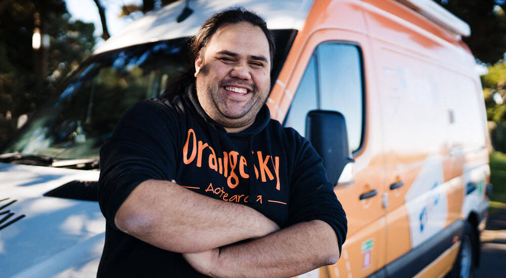 Orange Sky worker leaning against an Orange Sky mobile laundry van